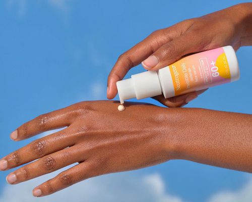 person applying sunscreen to back of hand against sky background