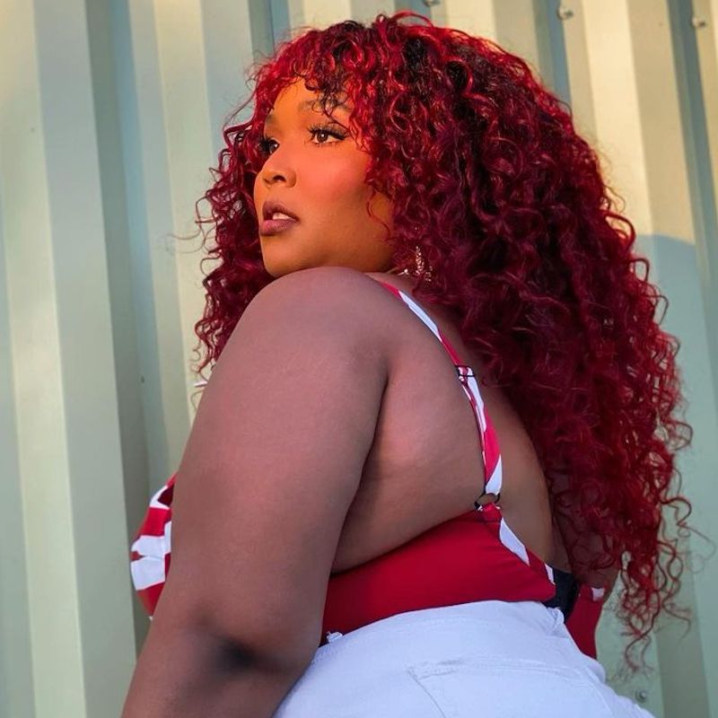 Lizzo wears a long, curly bright red hairstyle with bangs