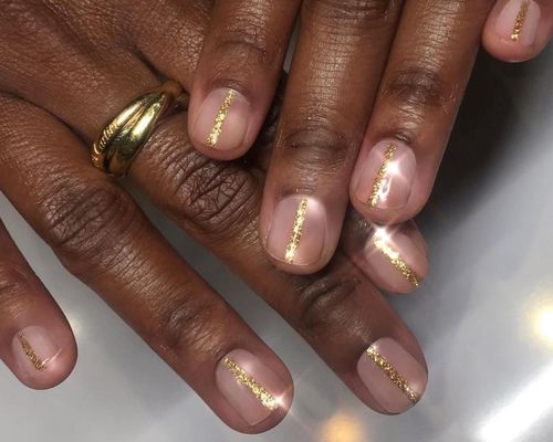 Close-up of manicure with neutral base and gold glitter central stripes