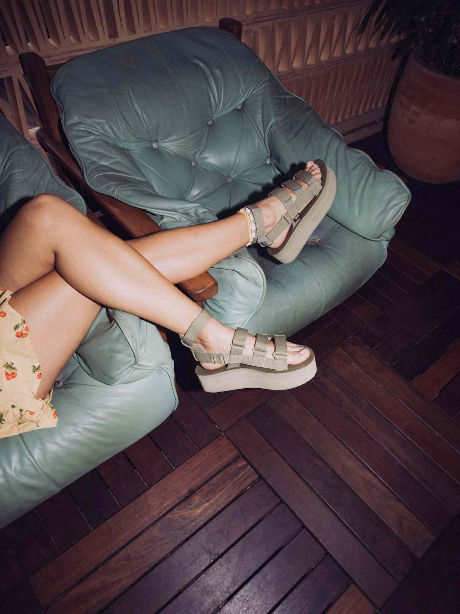 Person wearing Teva slingback platform sandals and cherry-patterned outfit while lounging on green chairs