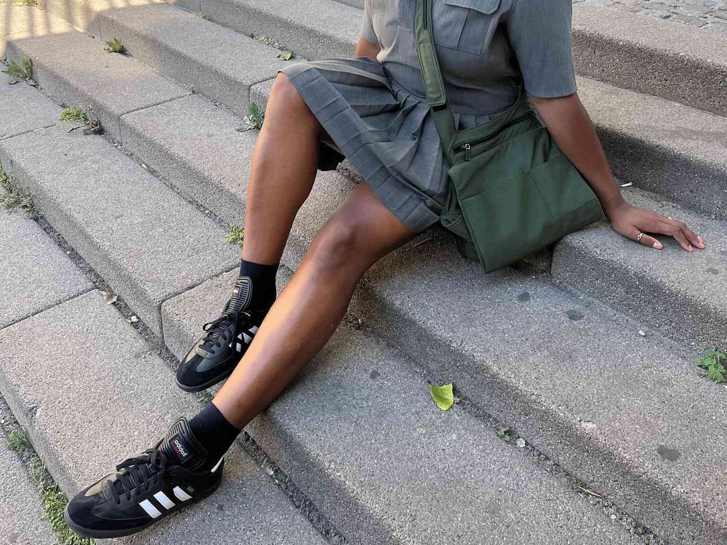 Influencer Imani Randolph wearing black Adidas Samba sneakers with a gray skirt and a green crossbody bag