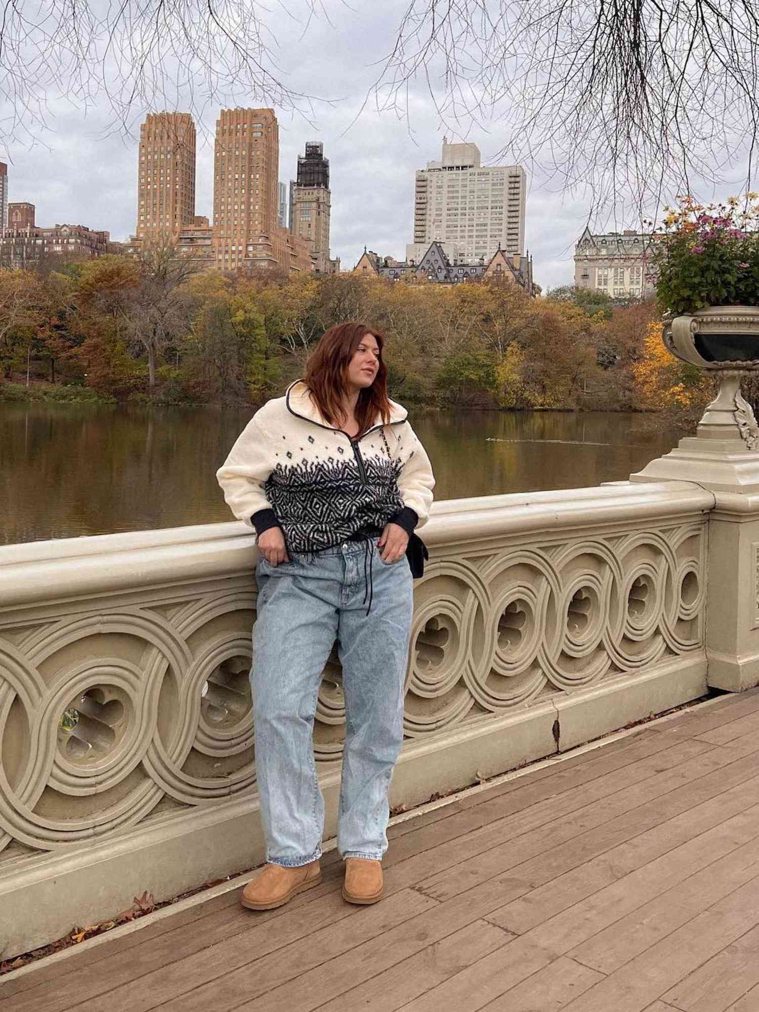 Raeann Langas wears a black and white patterned half-zip top, baggy jeans, and tan Ugg boots while standing on a bridge