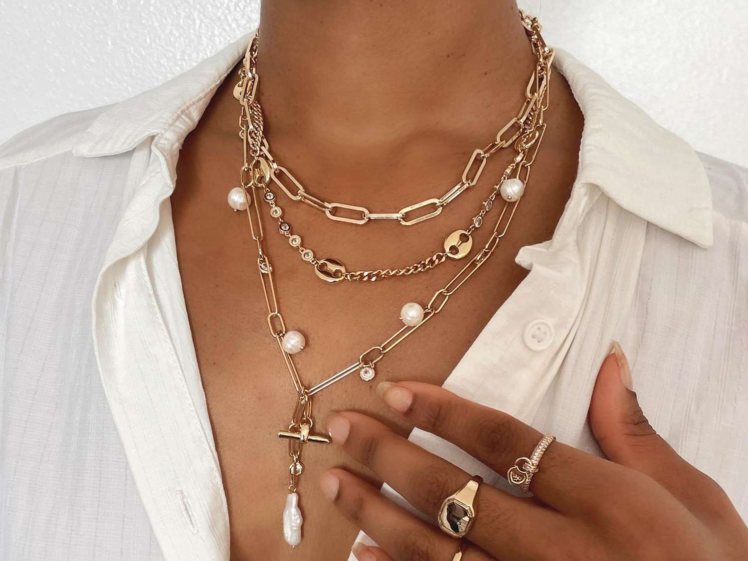 Close-up of woman wearing layered necklaces, rings, and white button-down shirt