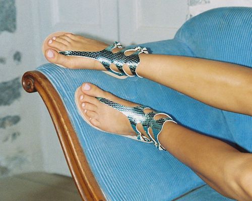 Feet wearing metallic scaly sandals and white gel pedicure on blue couch