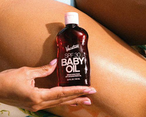 Close-up of woman holding bottle of Vacation sunscreen oil against oiled leg