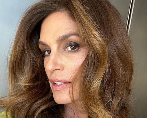 Cindy Crawford wears a subtle makeup look with foundation, pink lipstick, and a brown smoky eye