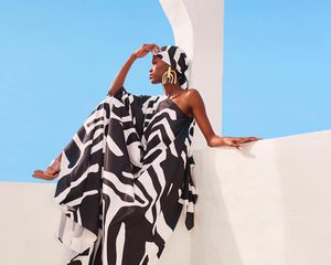 Woman sitting on balcony in sunshine wearing black and white dress and headscarf