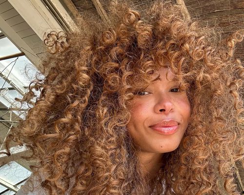 Woman with curly ginger hair, radiant skin, and glossy lips