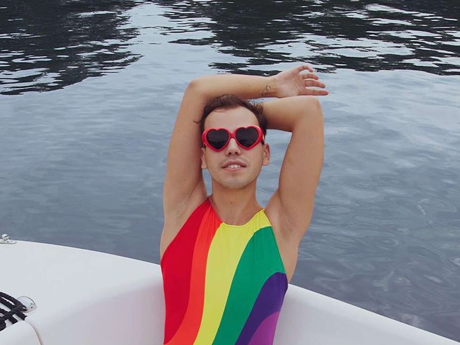 Person wearing rainbow swimsuit and heart-shaped sunglasses while on boat