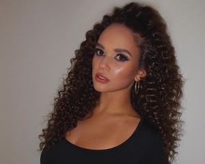 Actor Madison Pettis with her curly hair in a high ponytail, standing against a white wall