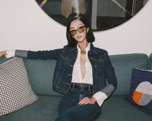 Chriselle Lim wears a denim jacket, jeans, and unbuttoned white button-down with tinted oversized sunglasses