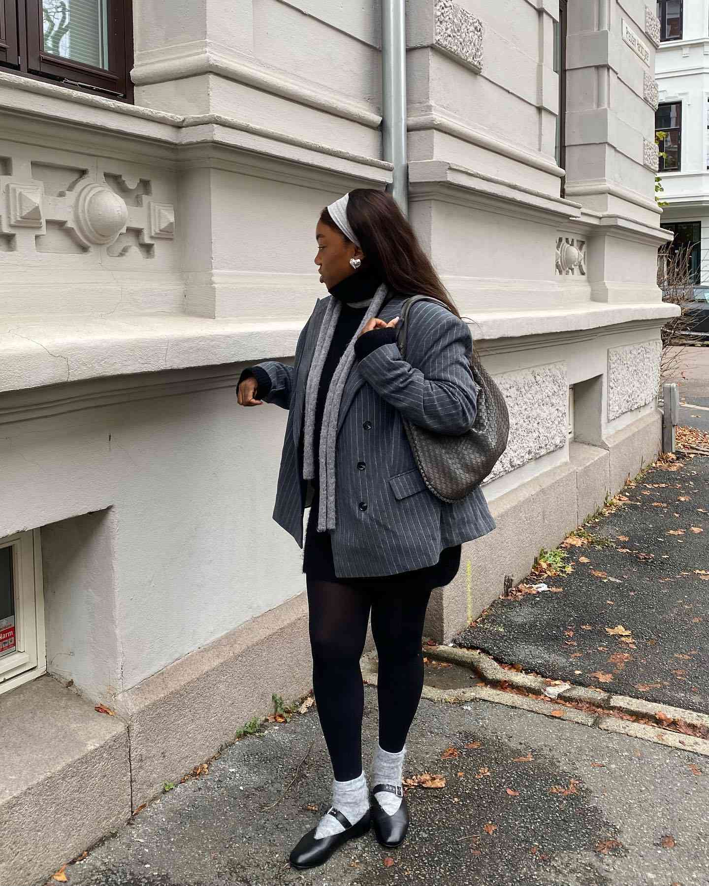 Nnenna Echem wears a gray pinstriped blazer, scarf, black turtleneck, white headband, black leggings, gray crew socks, and black ballet flats