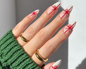 Close-up of manicure with neutral pink base, white French tips, and red gift wrap bow designs