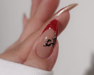 Close-up of manicure with red and gold glitter French tips and black dragon nail design