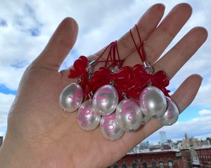 Hand holding Sandy Liang dragon egg charms against blue sky background