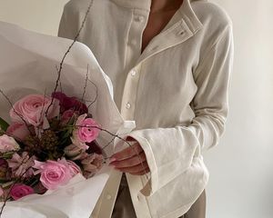 Close-up of woman wearing white button-down shirt and holding pink flowers