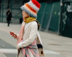 Linda Cui Zhang wears a beige trench coat, colorful knit sweater and scarf, and colorful fuzzy hat