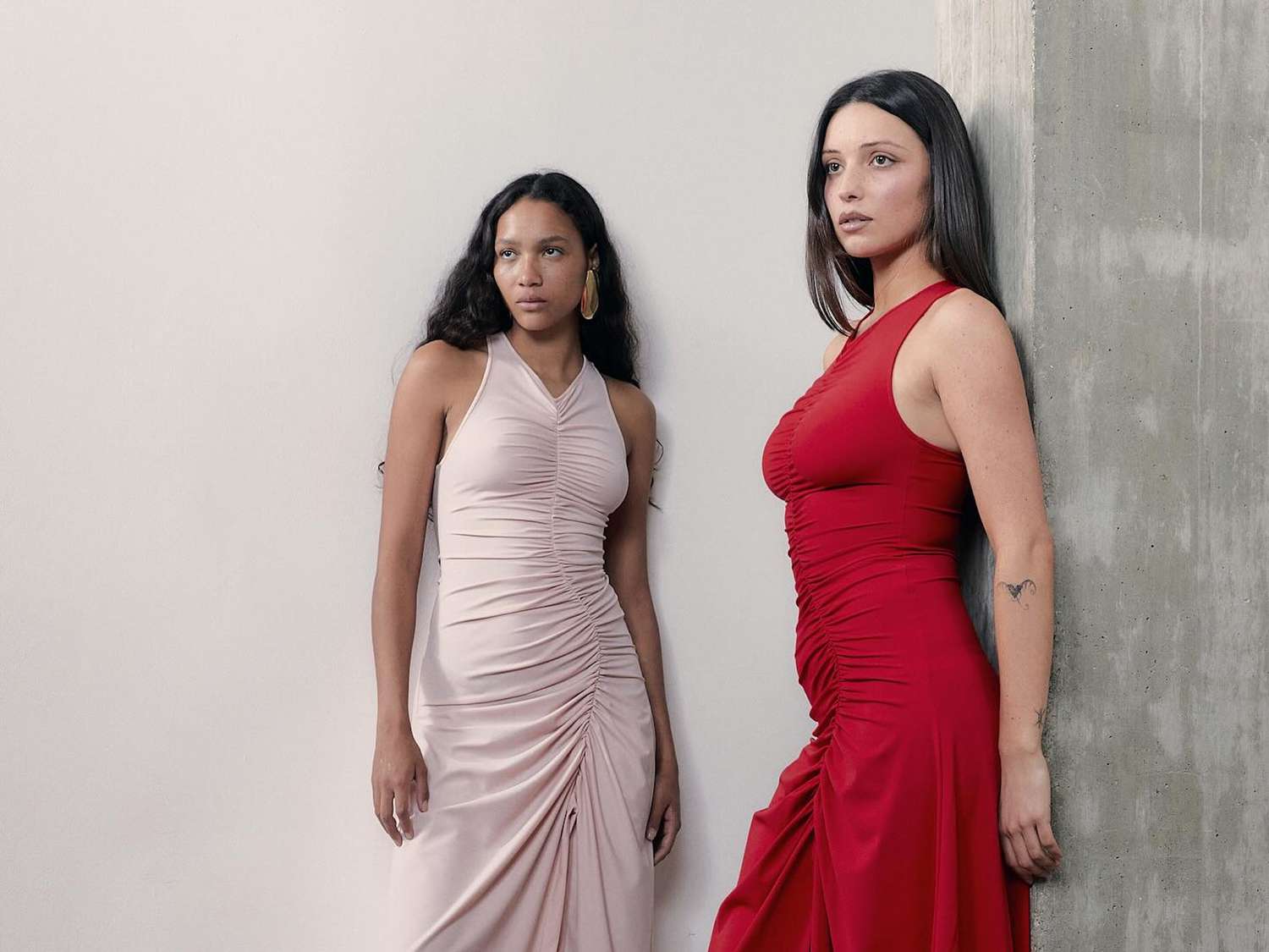 Two models wearing ruched red and pink dresses by Lamara London