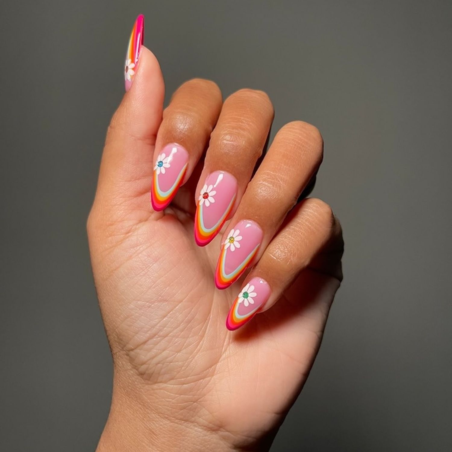 Hand with pink manicure with rainbow arched French tip and daisy nail stickers with colorful centers