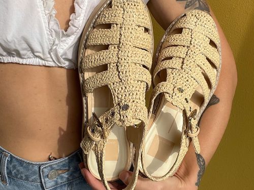 Close-up of woman holding woven fisherman sandals while wearing white crop top and jeans