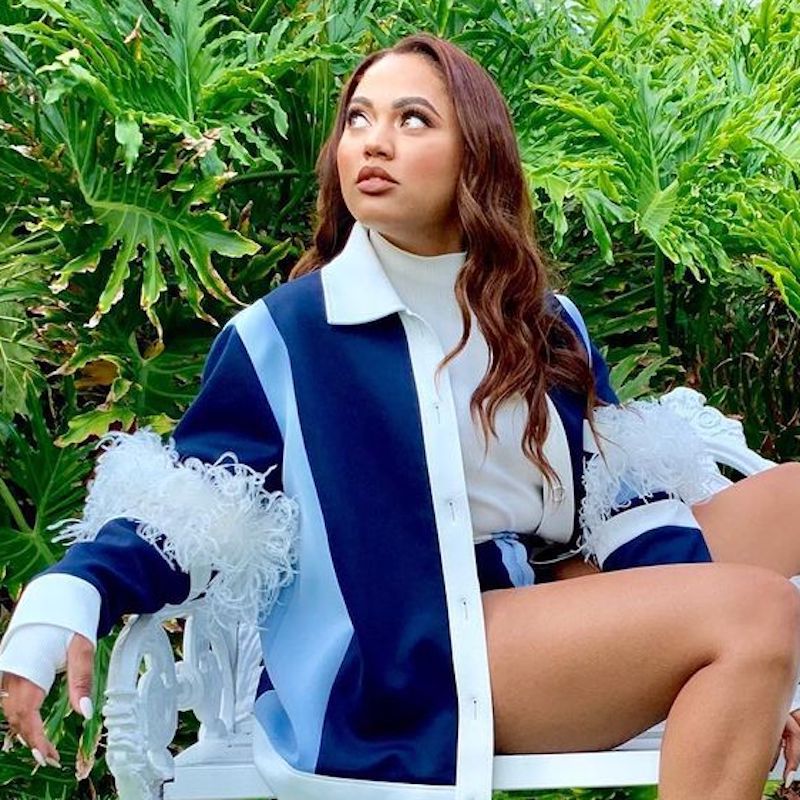 Ayesha Curry wears curled dark copper red hair and a blue color block jacket