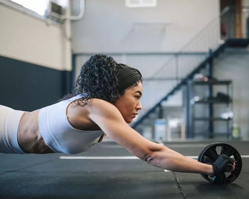 Woman in white sports set using ab roller