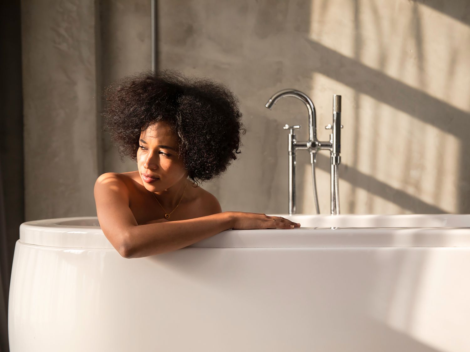 A woman is sitting in a bathtub. There are shadows on the wall.