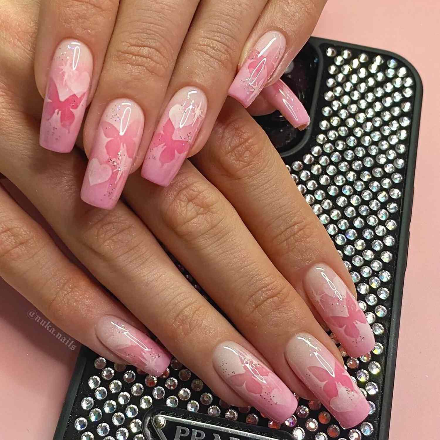 A baby pink manicure with butterfly designs