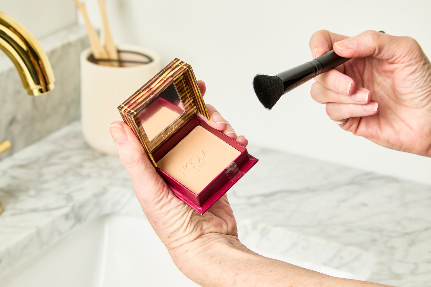 A person applies Benefit Cosmetics Hoola Bronzer with a makeup brush