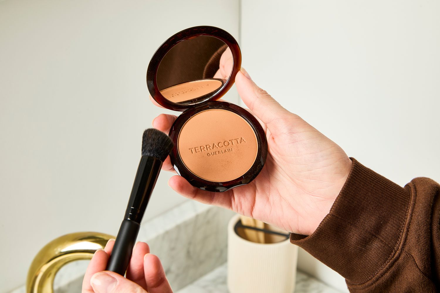 A person uses a makeup brush to apply Guerlain Terracotta Original Bronzing Powder