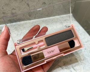 A person holds up the Tarte Big Ego Brow & Root Camo Kit eyebrow powder