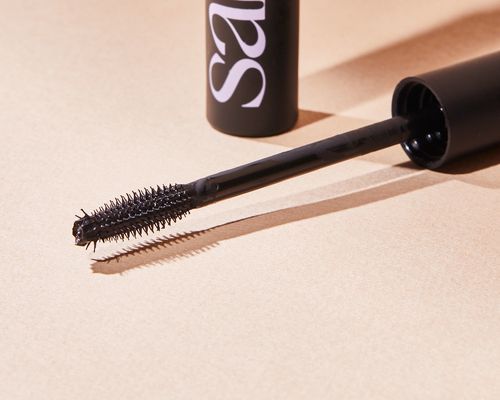 The Saie Mascara 101 wand next to the bottle on a light surface