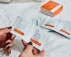 Hands holding Dr. Dennis Gross Universal Daily Peel packets with packaging displayed on marble countertop