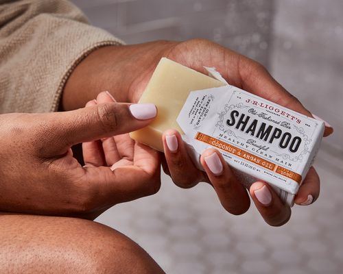 Hand pulling a J.R. Liggett's Coconut & Argan Oil Shampoo Bar from its box