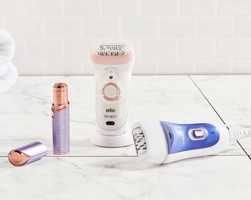 Three epilators, from Ramington, Braun, and Finishing Touch, displayed on a marble bathroom counter 