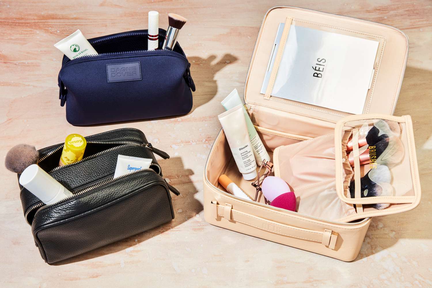 Three makeup bags sitting on a counter with makeup products inside them