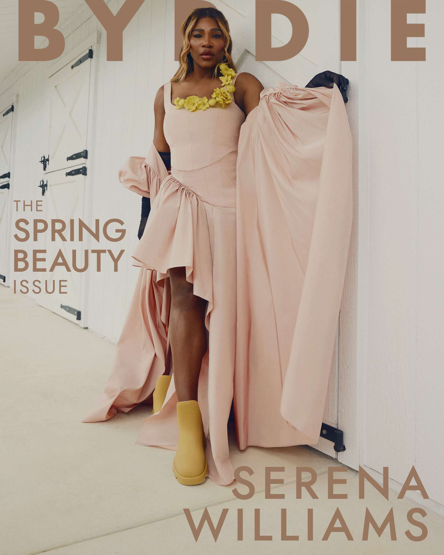 Serena Williams posing in a pink dress with yellow boots in front of white stables