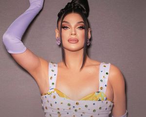 Valentina from drag race wears a bedazzled dress, lavender opera gloves, full glam makeup, and an updo hairstyle