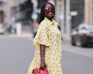 Woman wearing pastel yellow patterned tiered dress, oversized sunglasses, and pink handbag