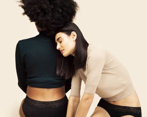 Two women knealing wearing Thinx underwear, one leaning on the other