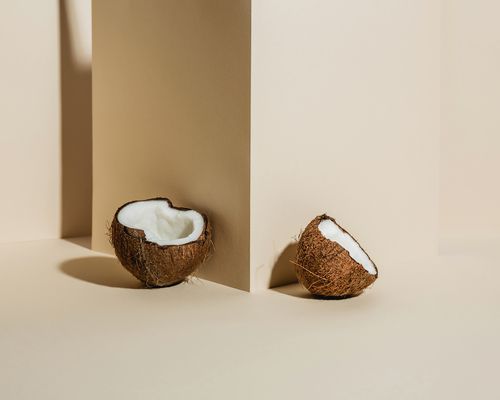 Two open coconut halves against a beige pillar on a beige floor