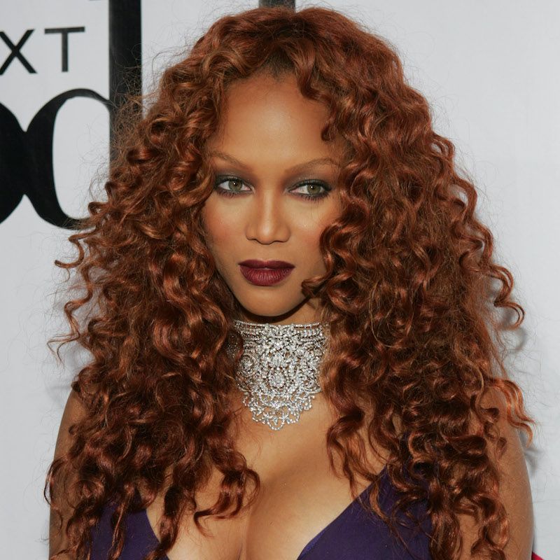 Tyra Banks wears a curly auburn copper hairstyle and burgundy lipstick