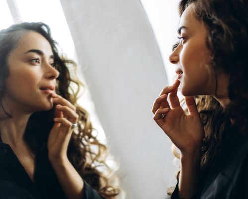 Woman touching her lips, looking in a mirror.