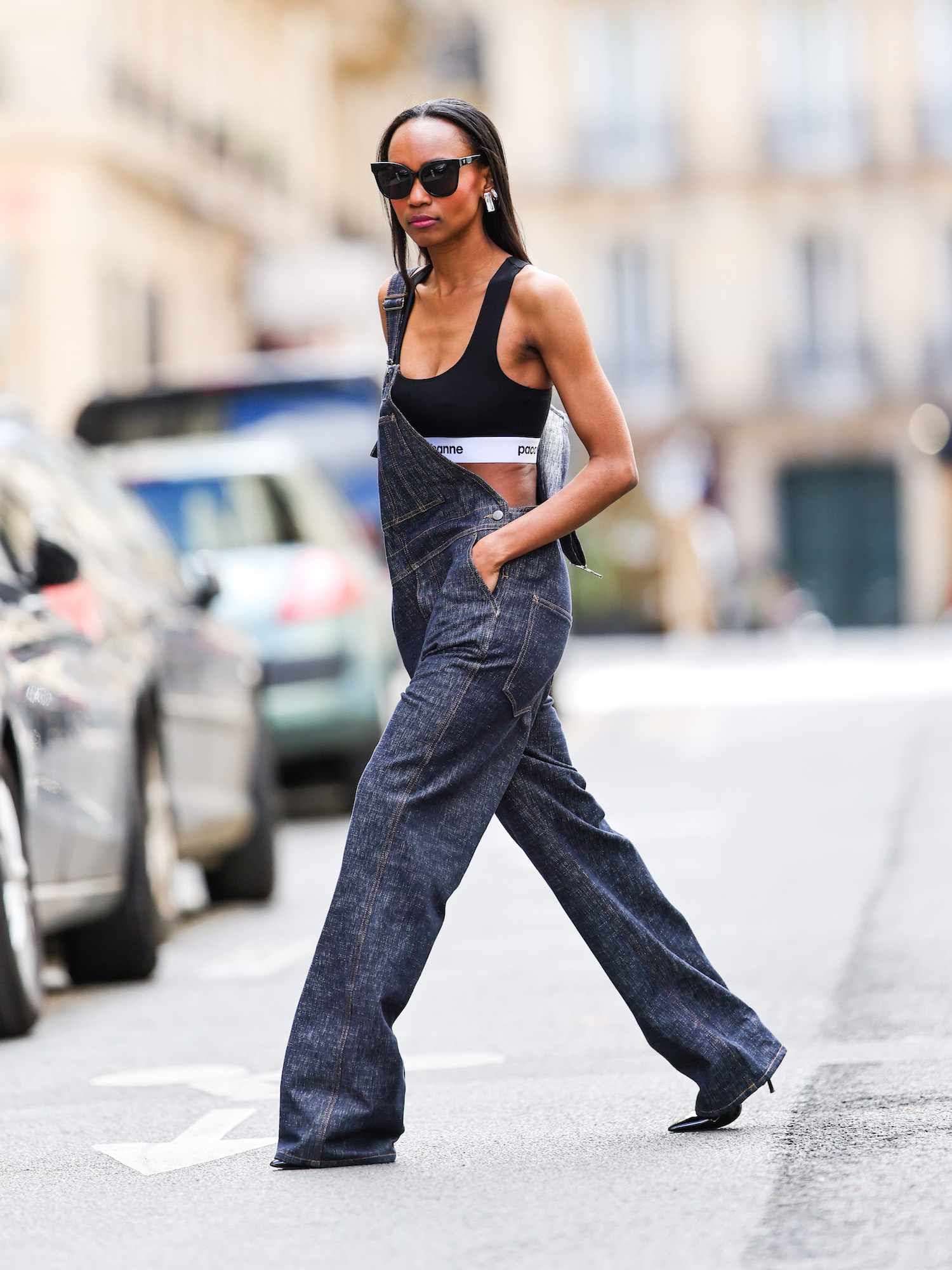 Emilie Joseph wears denim overalls, a Paco Rabanne logo sports bra, oversized sunglasses, and kitten heels