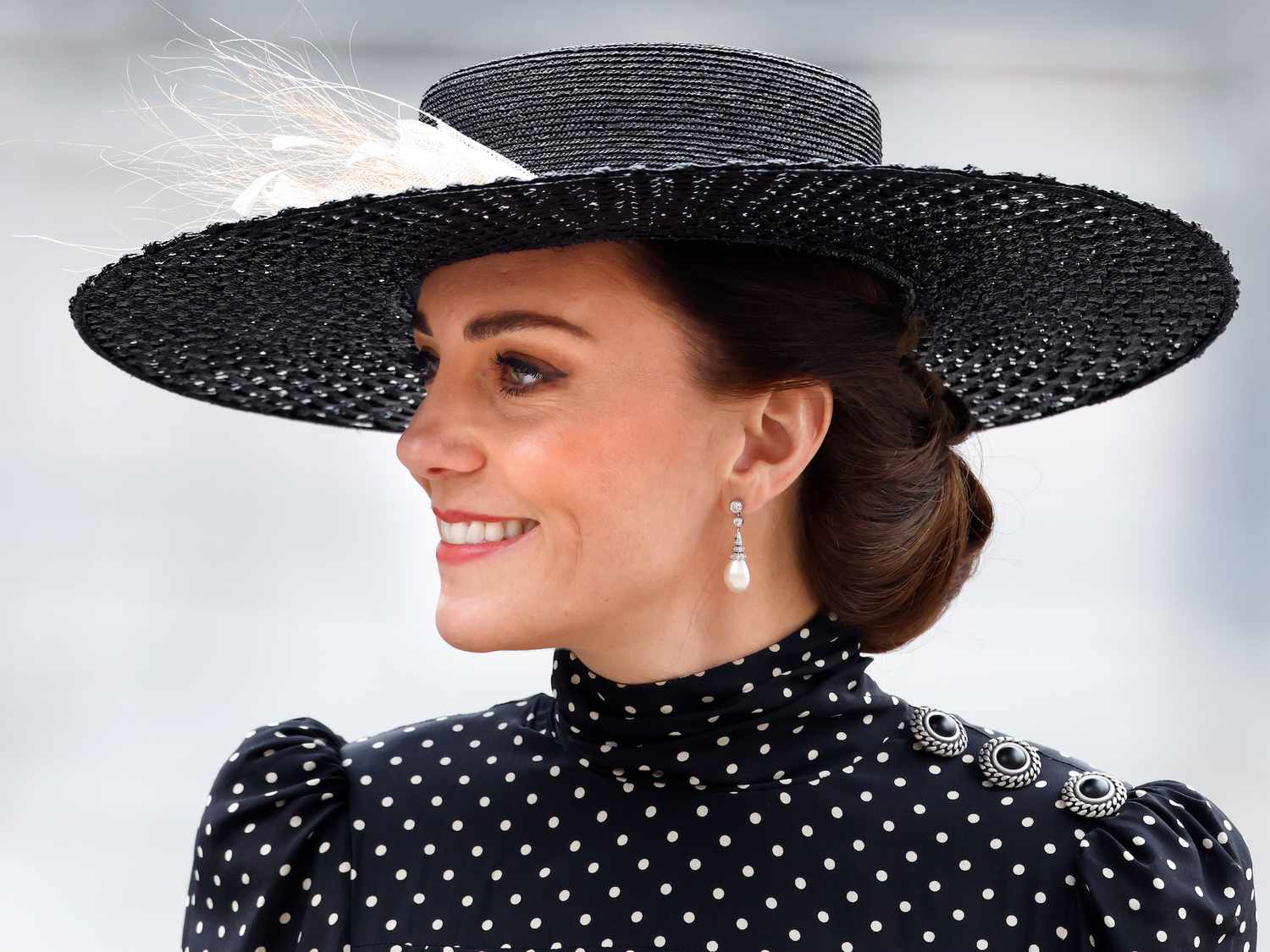 Kate Middleton wears a radiant makeup look, updo hairstyle, pearl drop earrings, black hat, and polka-dot dress