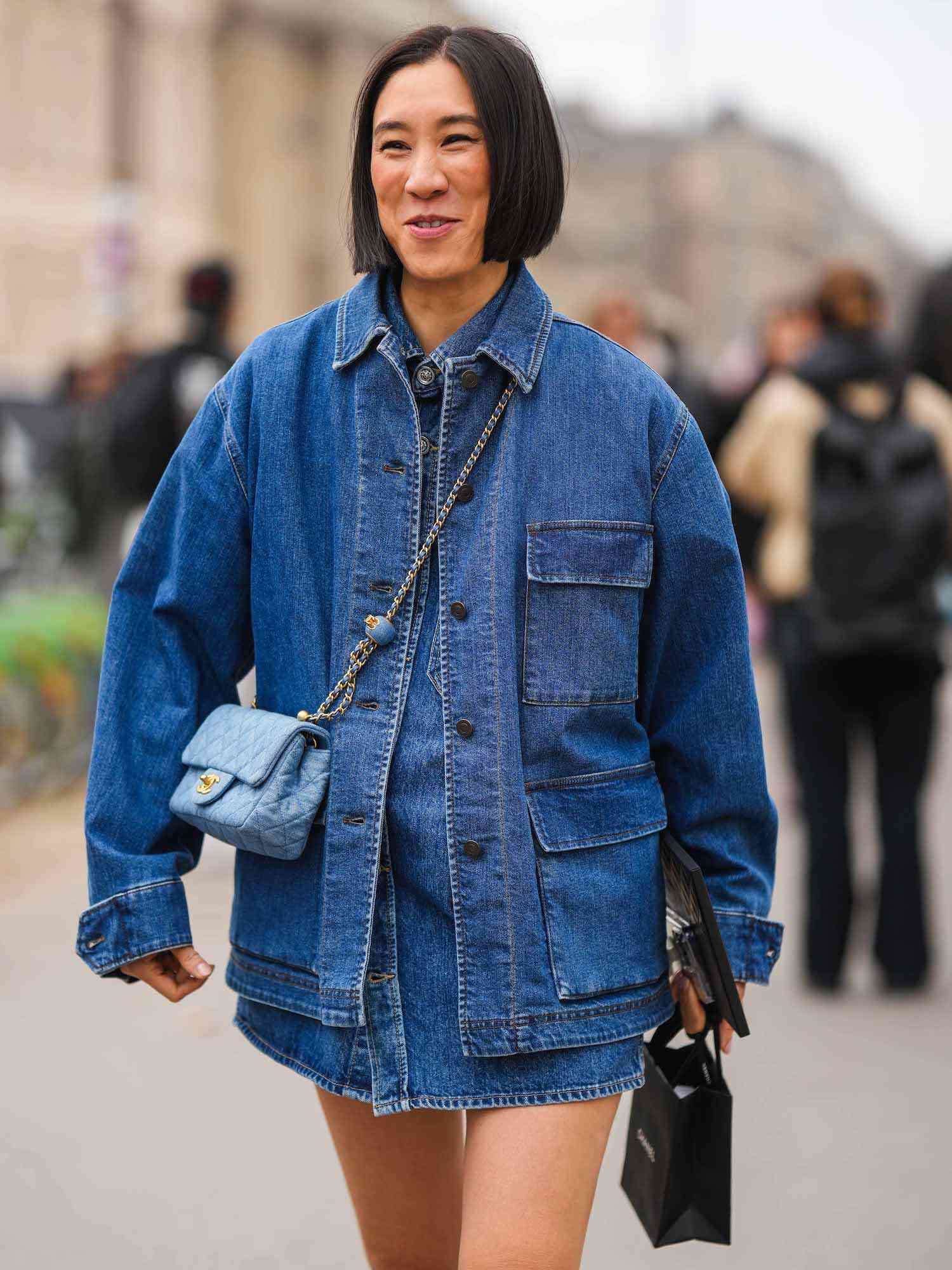 Eva Chen wears a denim cargo jacket, a button-down denim dress, a blue Chanel crossbody bag, and carries a Chanel shopping bag