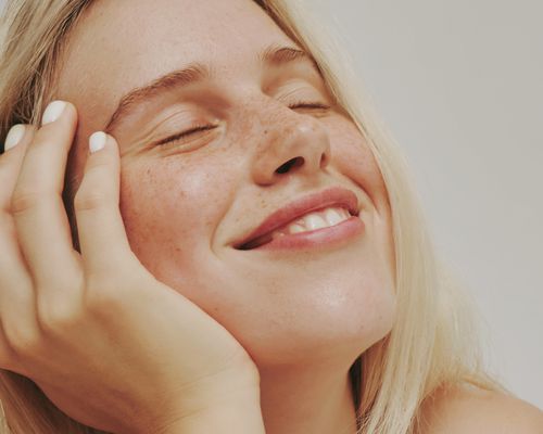 Blonde woman with freckles holding face and smiling