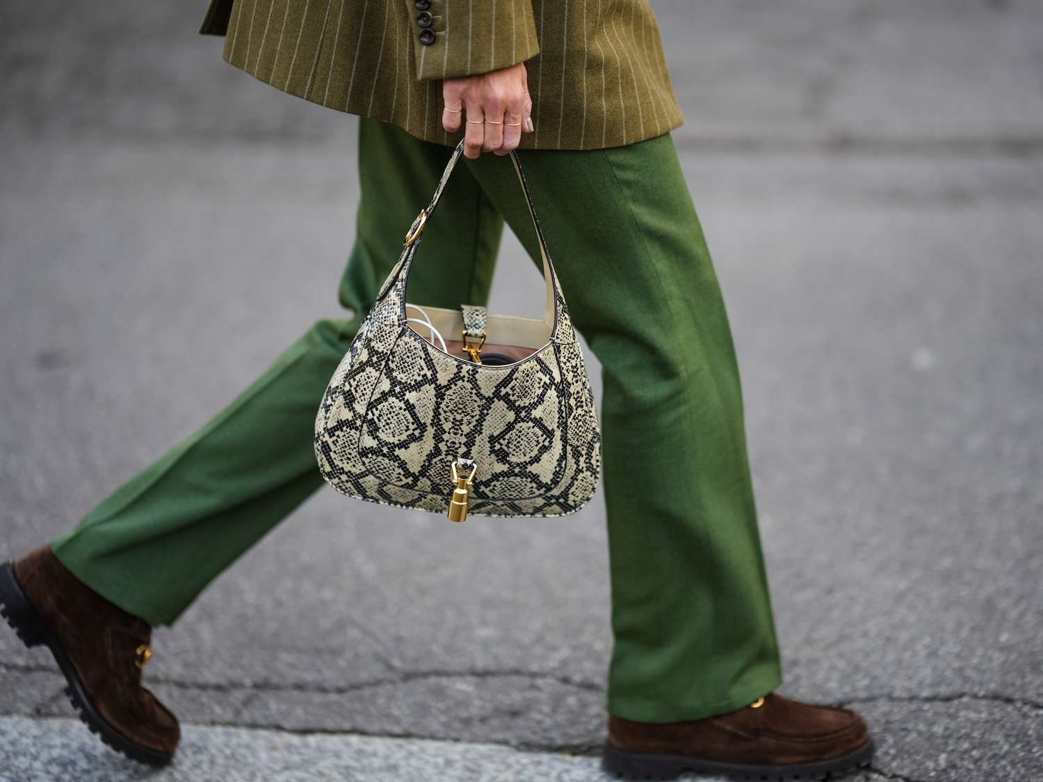 Close-up of woman wearing pinstriped blazer, green pants, brown loafers, and snake print Gucci handbag