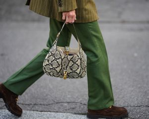 Close-up of woman wearing pinstriped blazer, green pants, brown loafers, and snake print Gucci handbag