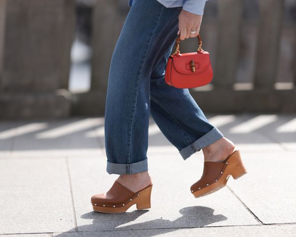 Close up of woman wearing brown studded clogs, cuffed jeans, and red handbag